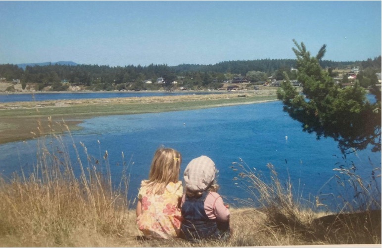 Two children sitting in the grass overlooking a lake
