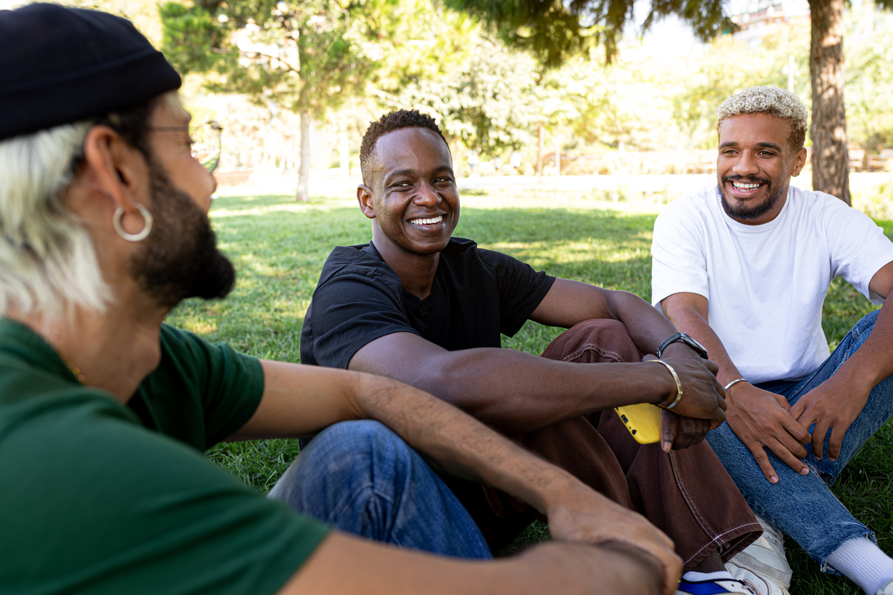 Three diverse individuals sitting on grass and smiling, symbolizing the sense of belonging and inclusivity in group learning experiences 