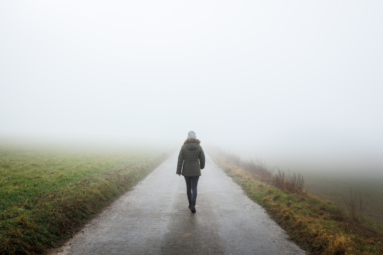 Woman walks on a misty road to unknown destination