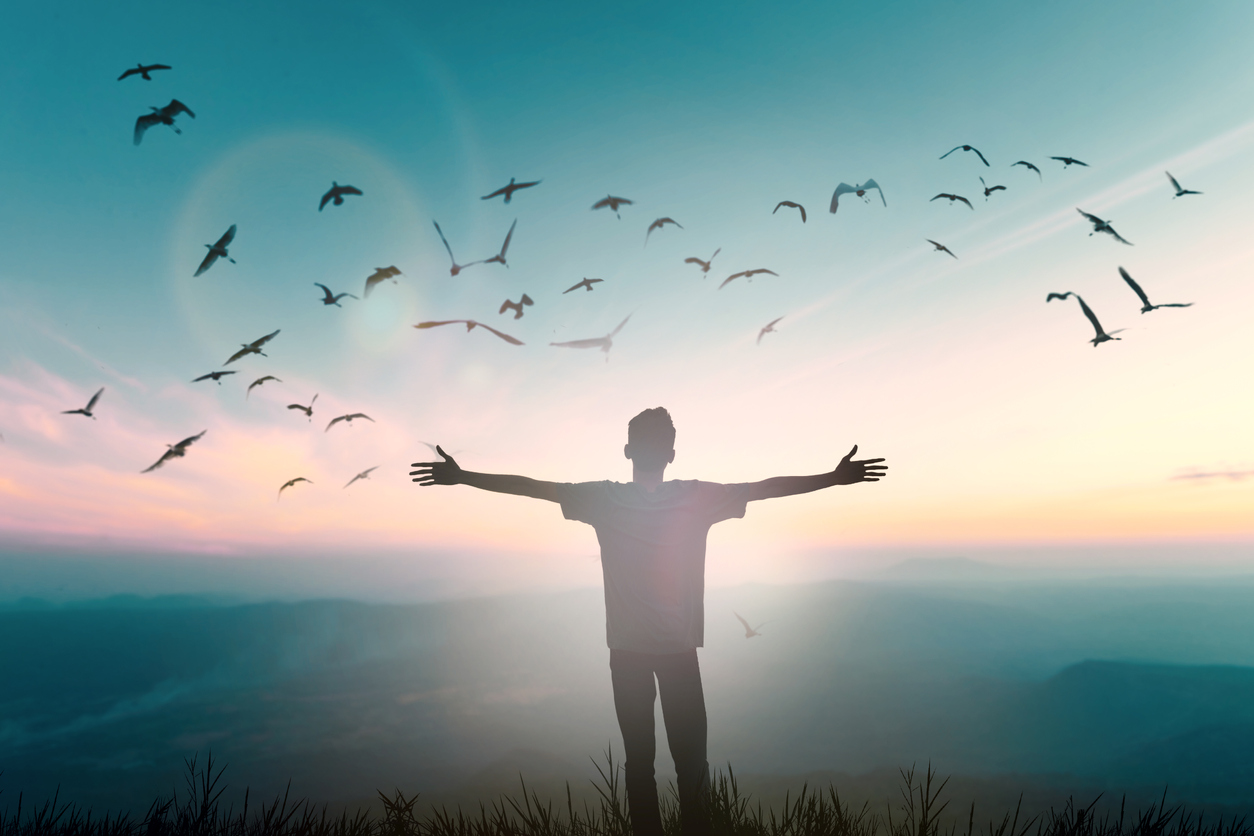 Man with arms outstretched on a hilltop at dawn, symbolizing freedom and new beginnings, akin to a life coach