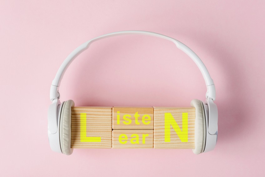 a pair of headphones around wooden blocks that spell “LISTEN” and “LEARN”