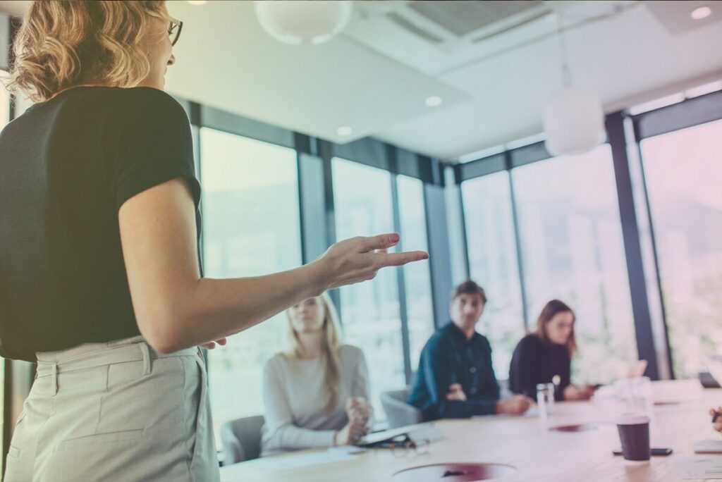 Learn how to become a certified coach to confidently lead others and effect positive change as the woman in this conference room is doing.