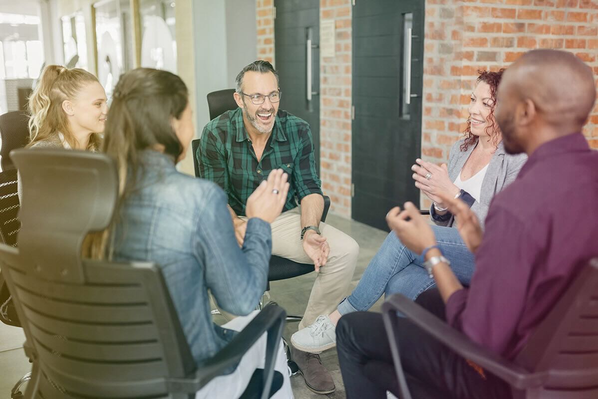 A group of adults smiles and converses in an open-office business setting as they build rapport.