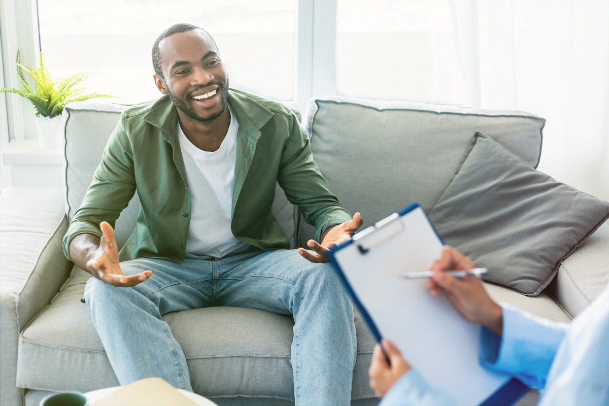 man sitting on couch talking to person with clipboard