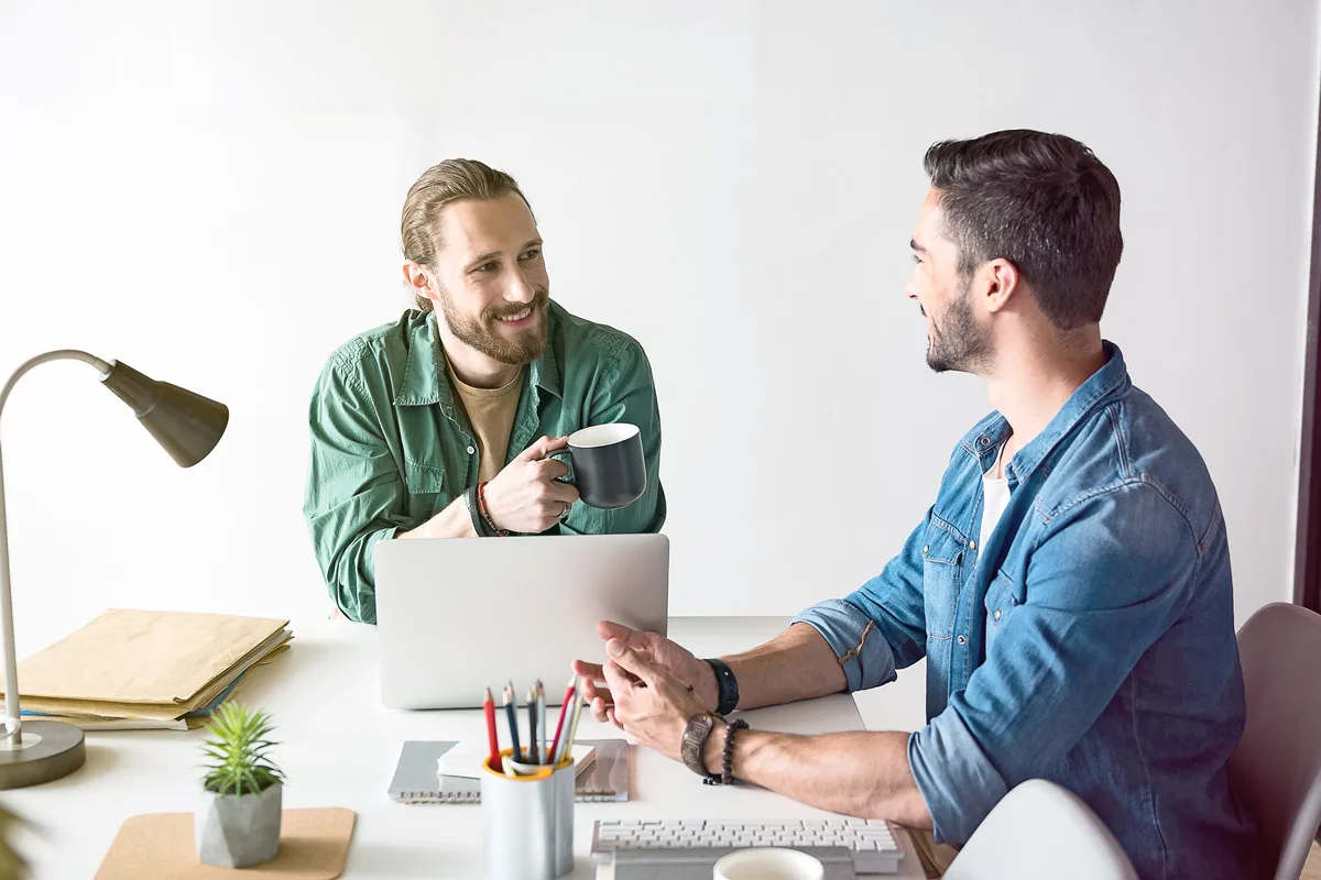 two men having conversation with laptop and coffee