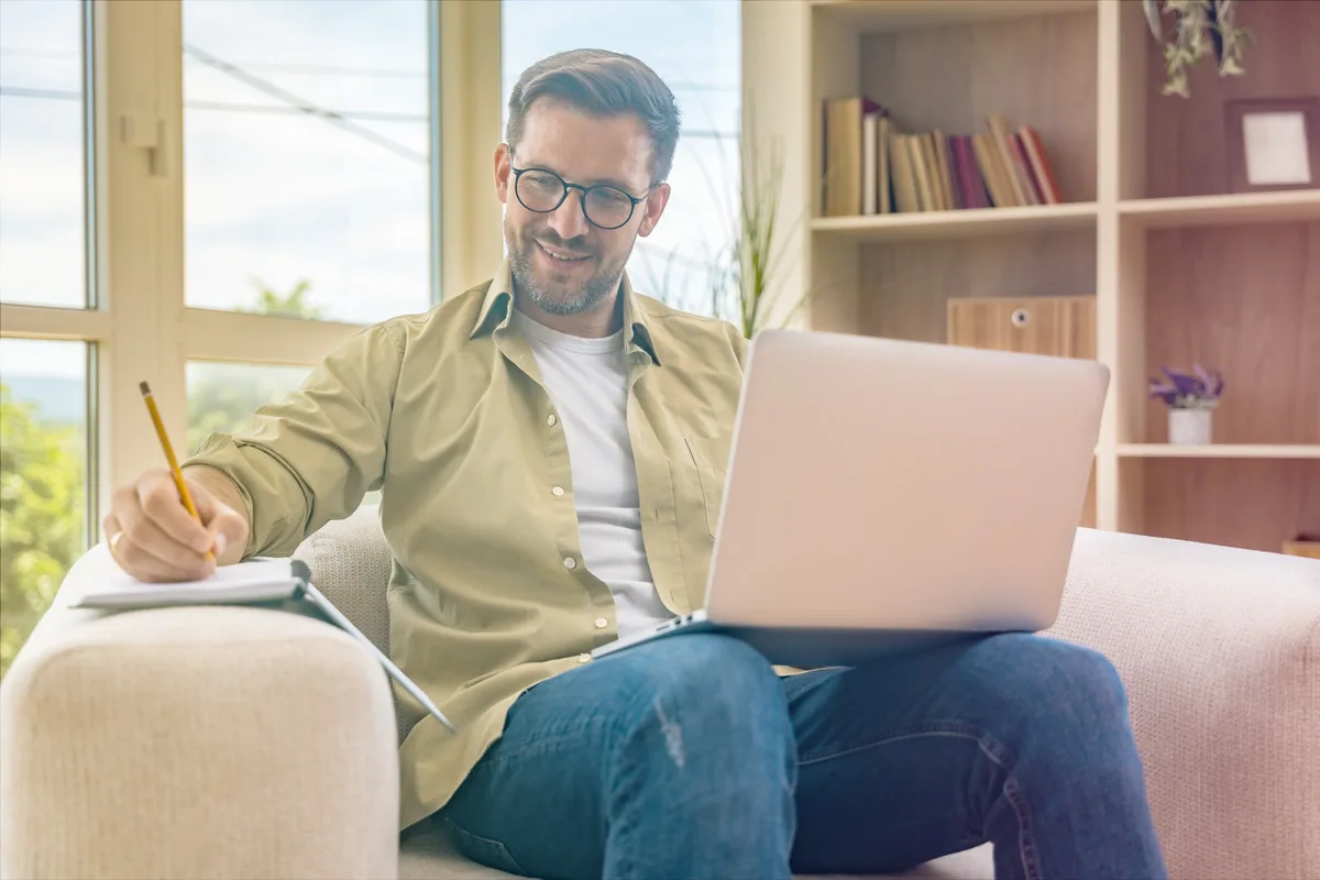 Professional taking notes while working on laptop at home