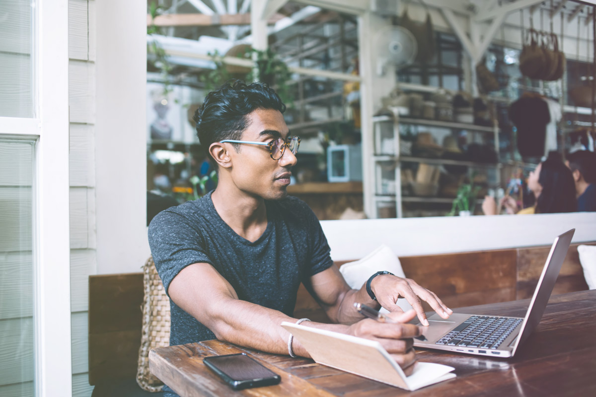 Professional preparing notes while working on laptop in café