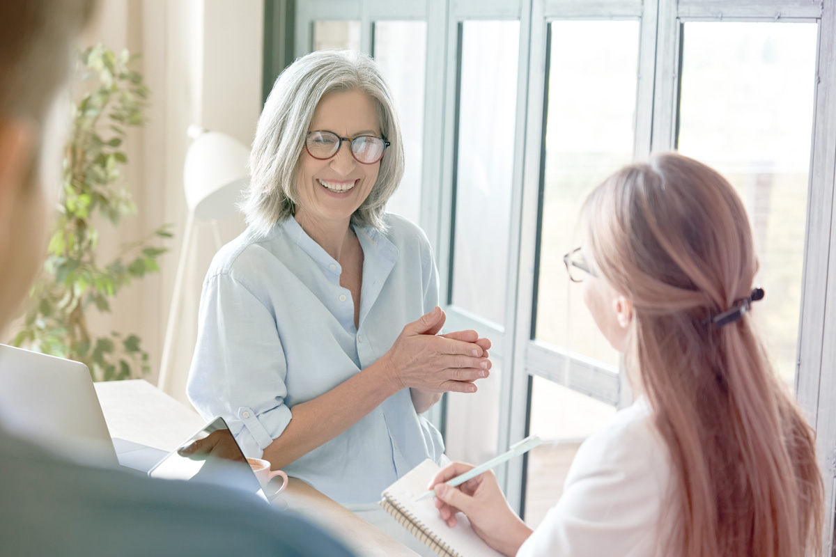 Lady in white shirt standing next to a window smiling