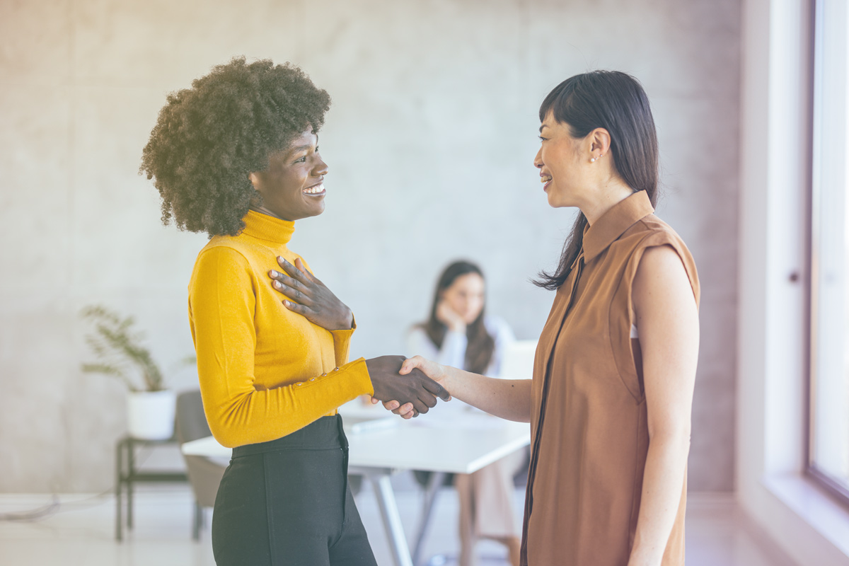 Two women smiling and shaking hands in a professional setting.