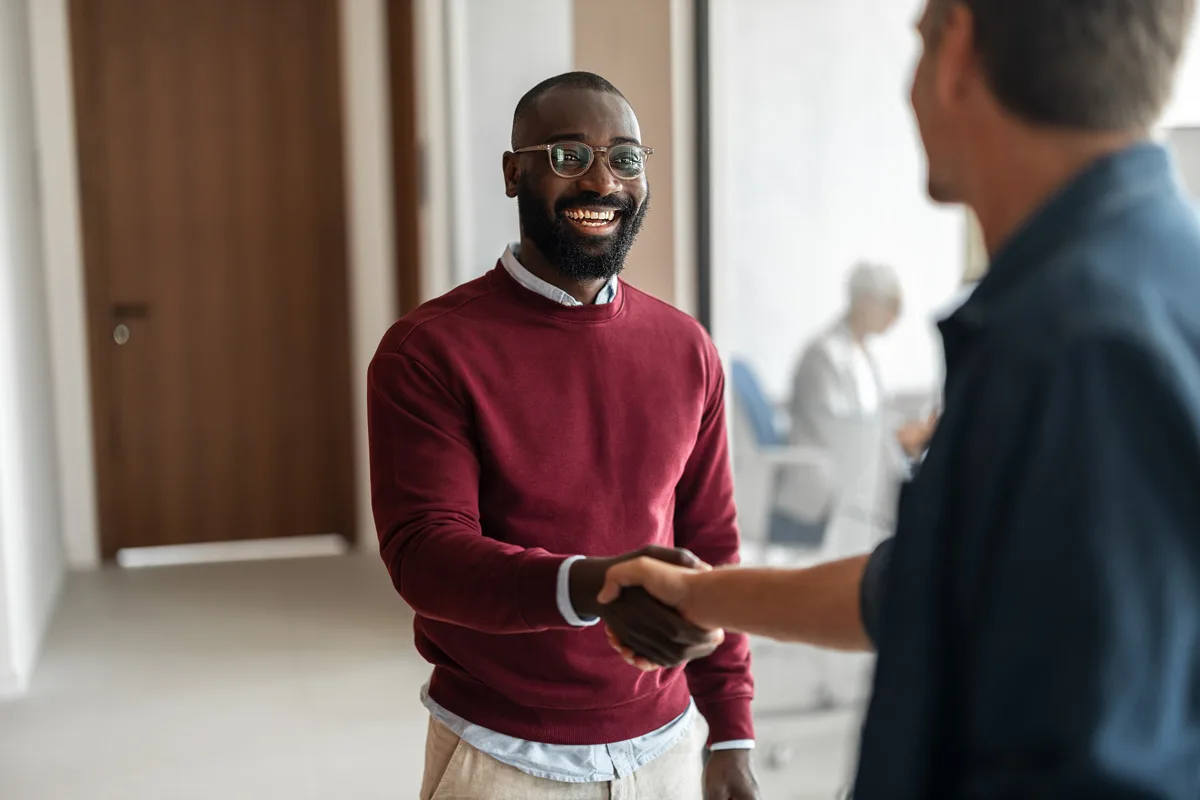 Two colleagues shaking hands in an office hallway.