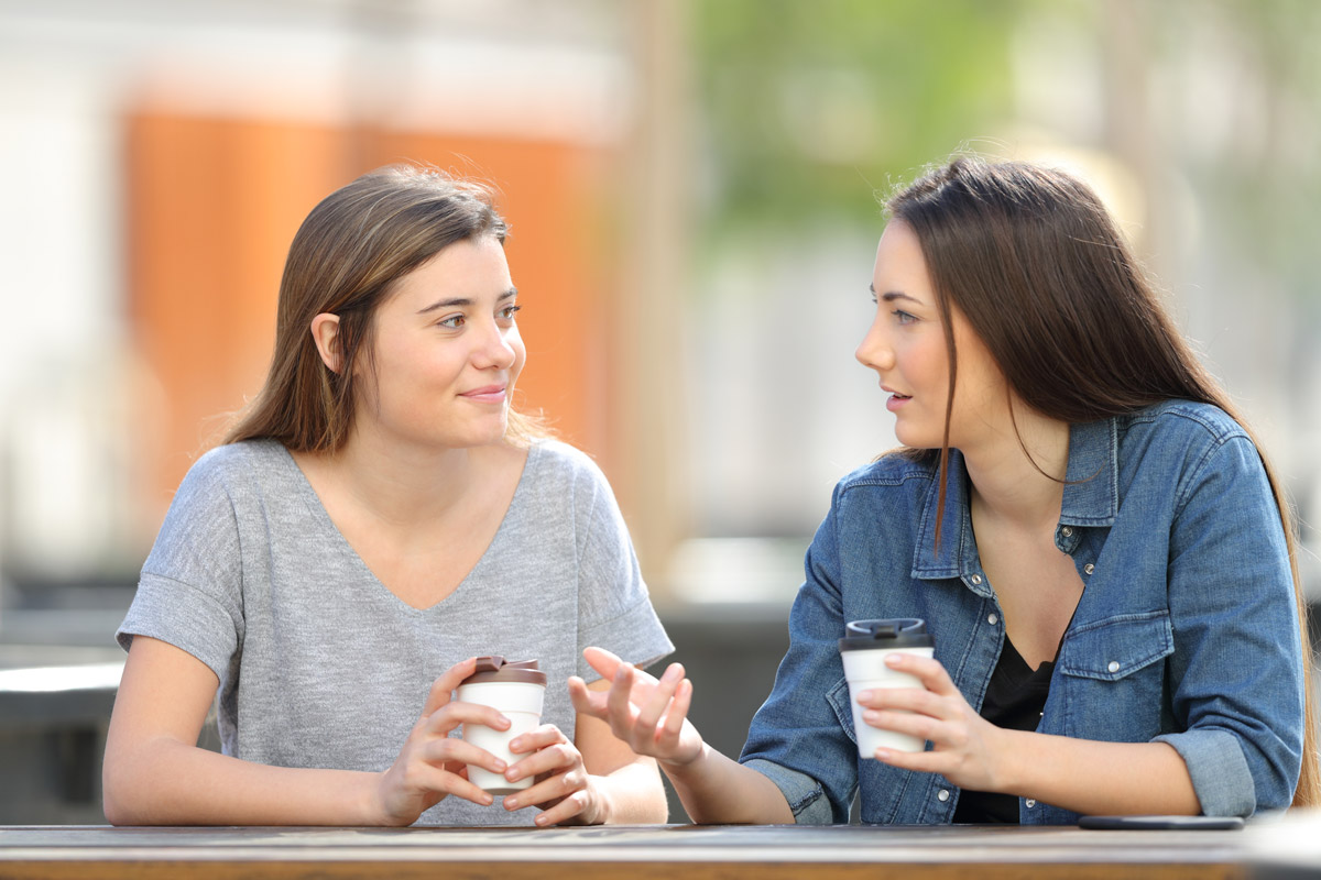 Two women talking over coffee at an outdoor table.