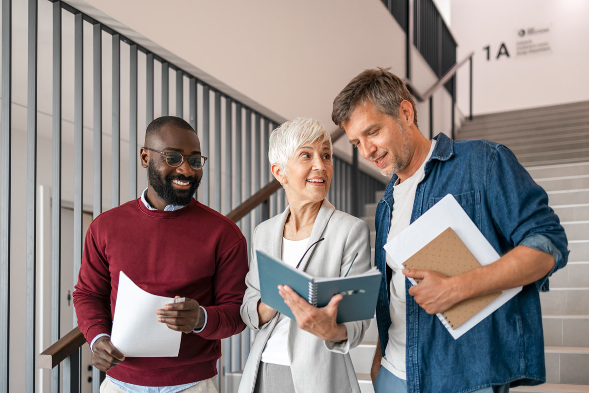 Three professionals discussing documents in an office hallway.