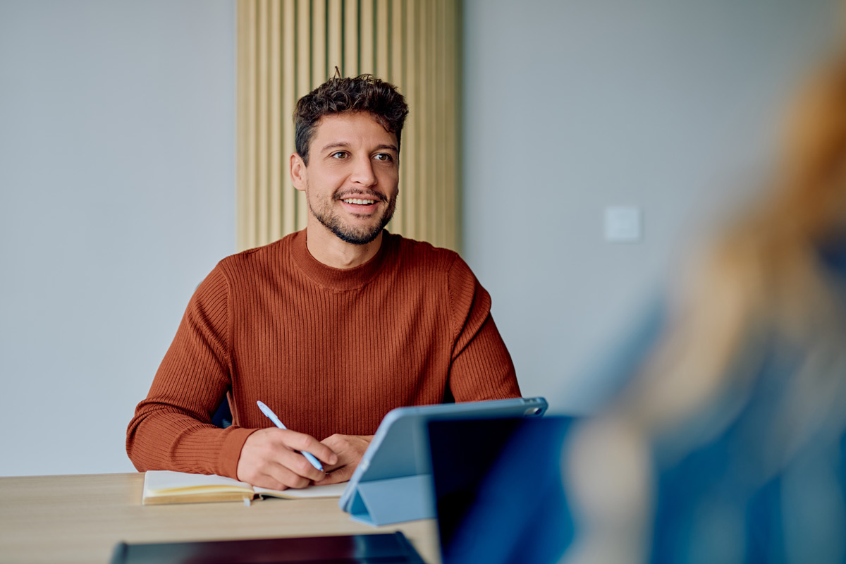 Man smiling while taking notes in a meeting.
