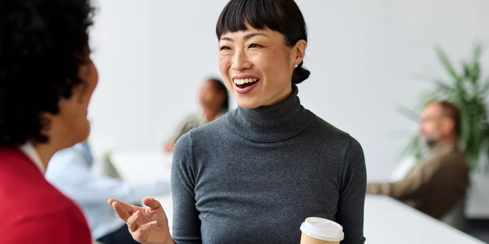 two female office workers discuss while looking at tablet