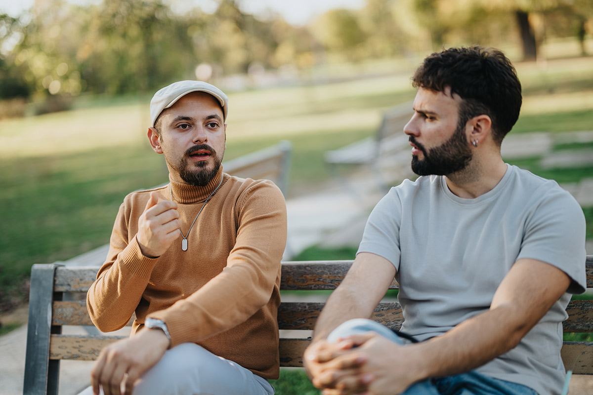 wo men talking while sitting on a park bench.
