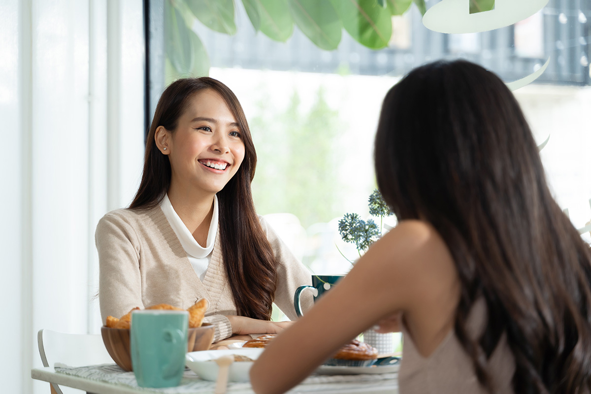 Two women smiling and talking while sitting at a table.